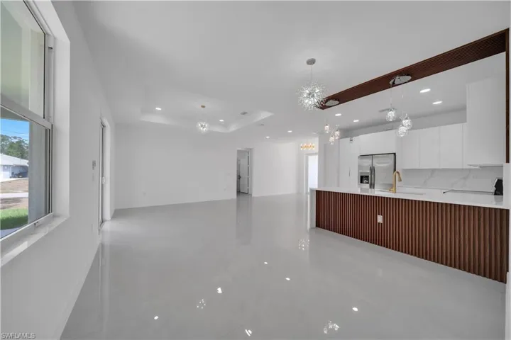Kitchen with a chandelier, stainless steel refrigerator with ice dispenser, white cabinets, a sink, and recessed lighting