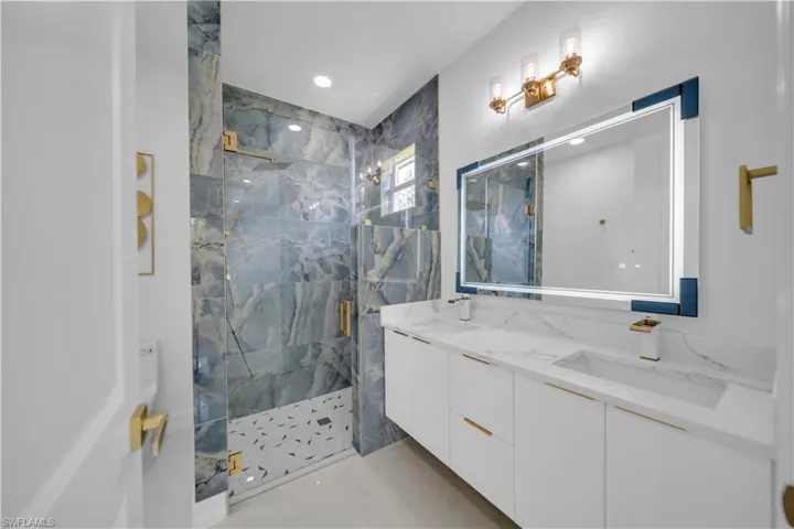 Bathroom featuring a marble finish shower, double vanity, and recessed lighting