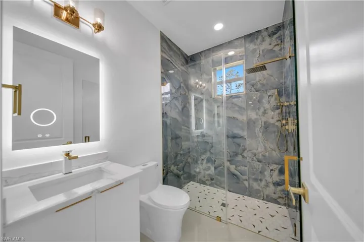 Full bath with toilet, a marble finish shower, vanity, and recessed lighting