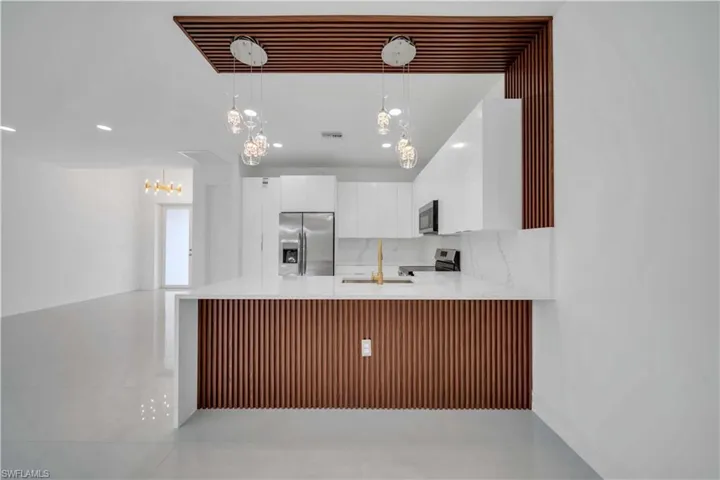 Kitchen with appliances with stainless steel finishes, a chandelier, a peninsula, white cabinetry, and a sink