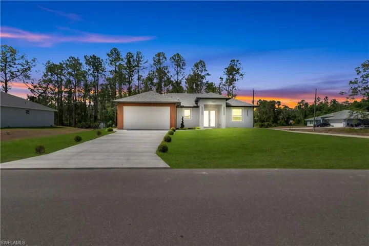 View of front of property featuring a garage, concrete driveway, a front yard, and stucco siding