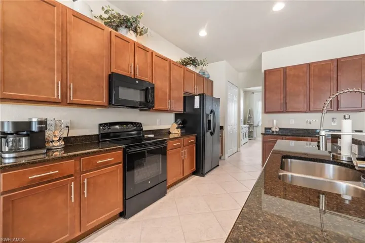 Kitchen with sink, black appliances, dark stone counters, and light tile patterned flooring