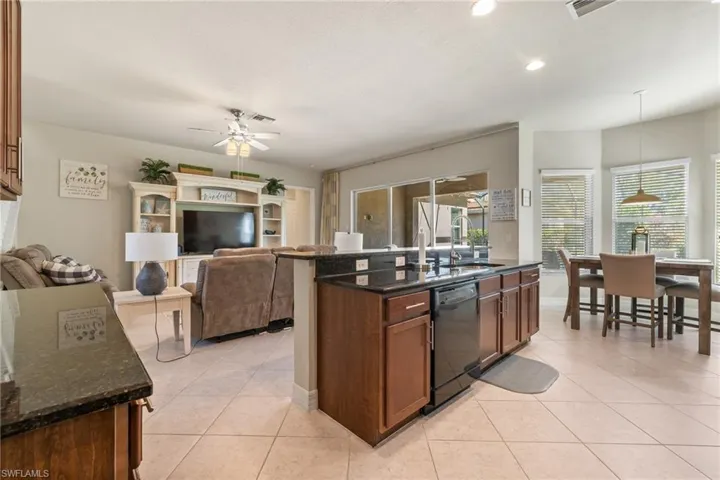 Kitchen with hanging light fixtures, dark stone countertops, black dishwasher, and sink