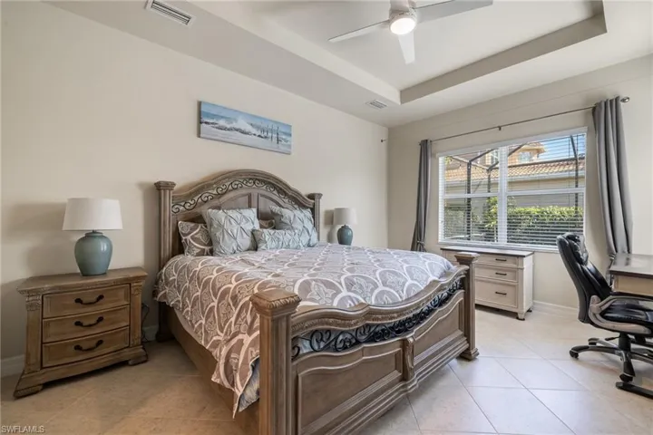 Tiled bedroom featuring a raised ceiling and ceiling fan