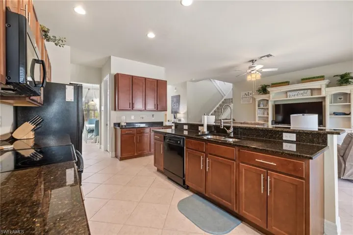 Kitchen featuring sink, light tile patterned floors, ceiling fan, dark stone counters, and black appliances