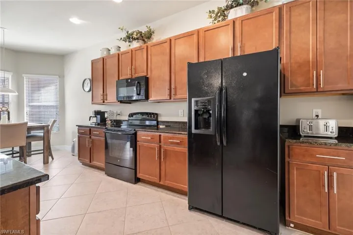 Kitchen with dark stone counters, light tile patterned floors, and black appliances