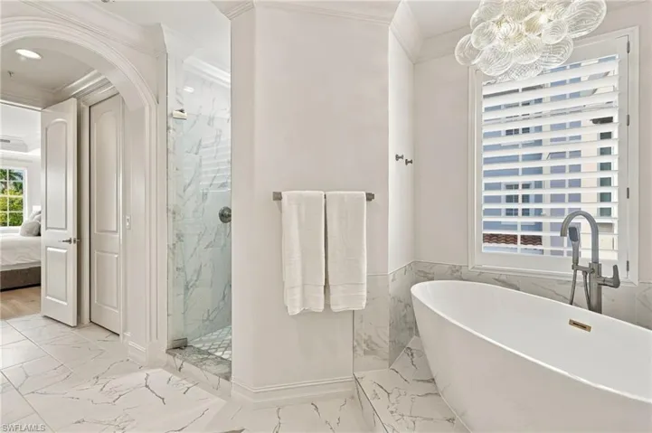 Freestanding soaking tub, walk-in shower with glass enclosure, marble-style tile flooring, and a decorative light fixture