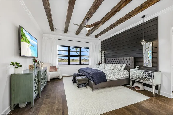 Bedroom with wooden walls, dark wood-style floors, beamed ceiling, ceiling fan, and an accent wall