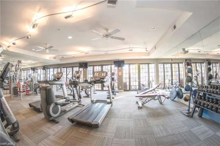 Exercise room with ceiling fan, carpet floors, rail lighting, and a raised ceiling