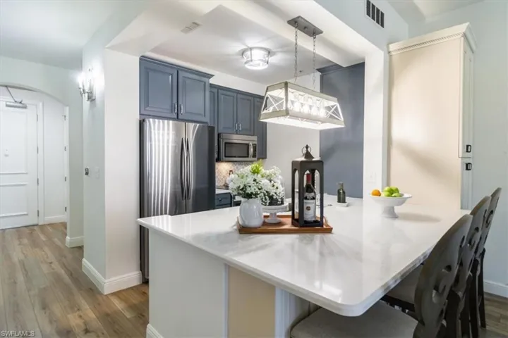 Kitchen with light hardwood / wood-style flooring, appliances with stainless steel finishes, kitchen peninsula, decorative light fixtures, and blue cabinets