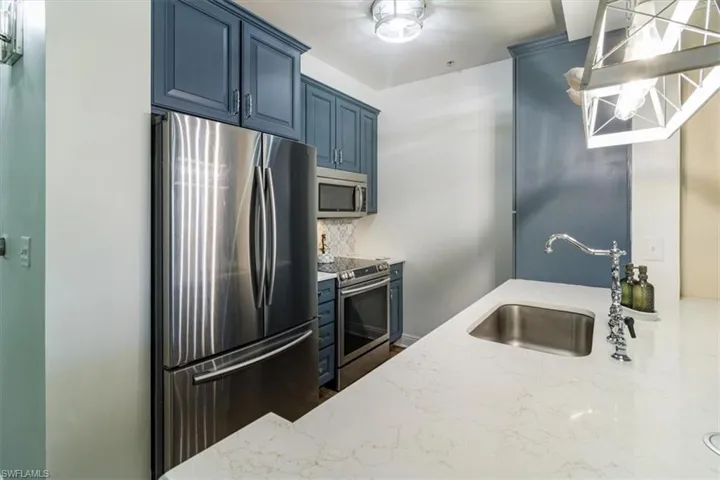 Kitchen featuring blue cabinets, stainless steel appliances, backsplash, and sink