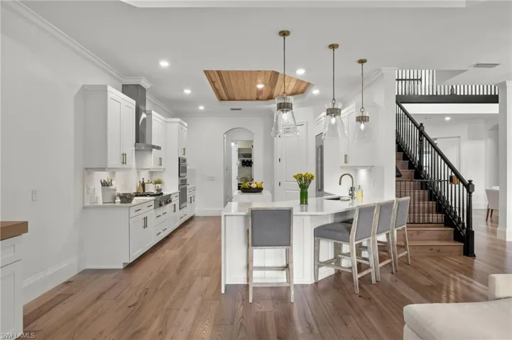 Kitchen with light hardwood / wood-style floors, white cabinetry, decorative light fixtures, and sink
