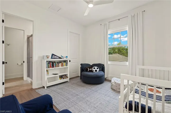 Bedroom with ceiling fan, wood-type flooring, and a crib
