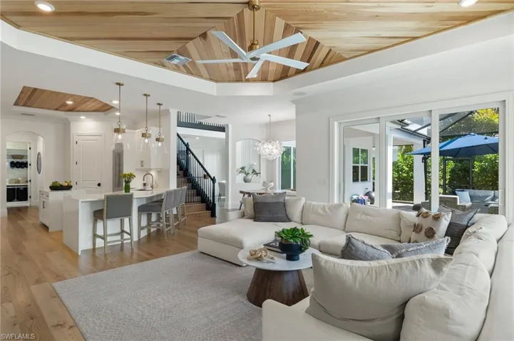 Living room featuring sink, ceiling fan with notable chandelier, wood ceiling, light hardwood / wood-style floors, and lofted ceiling