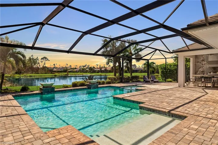 Pool at dusk with a patio area, an in ground hot tub, a water view, and glass enclosure