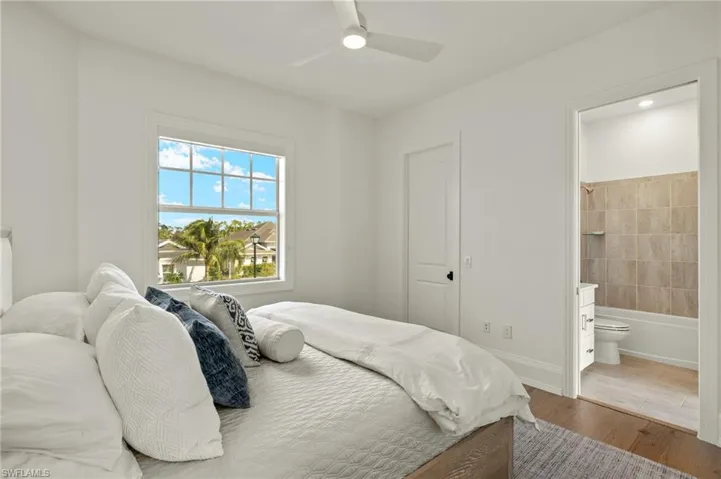 Bedroom with hardwood / wood-style floors, ceiling fan, and ensuite bath