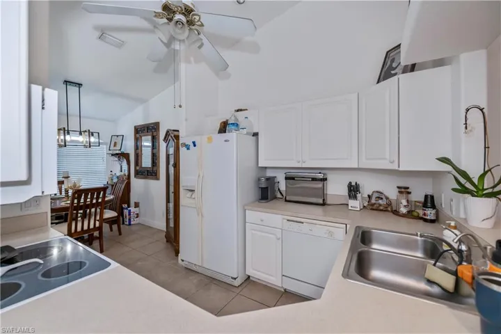 Kitchen with white appliances, lofted ceiling, ceiling fan, light tile patterned flooring, and white cabinetry
