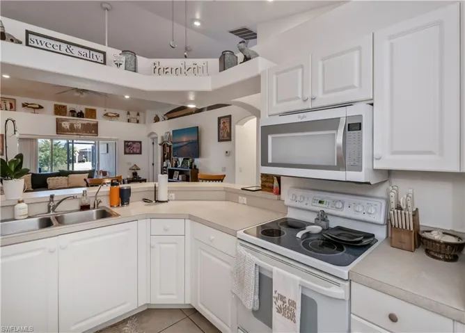 Kitchen with white appliances, a sink, white cabinets, and light countertops