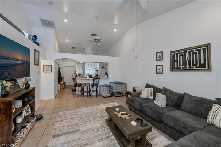 Living area with ceiling fan, light tile patterned flooring, arched walkways, and high vaulted ceiling