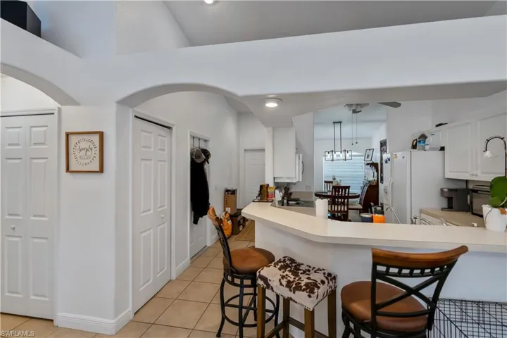 Kitchen with white fridge with ice dispenser, light tile patterned flooring, a kitchen bar, and white cabinetry