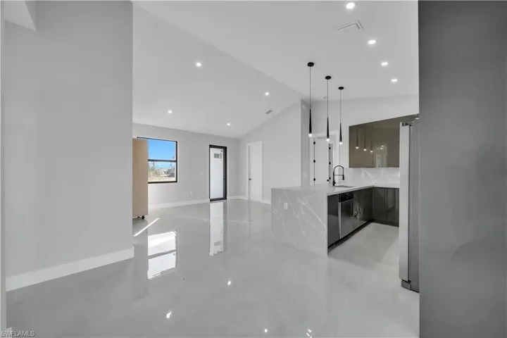 Kitchen with modern cabinets, light stone countertops, vaulted ceiling, stainless steel appliances, and hanging light fixtures