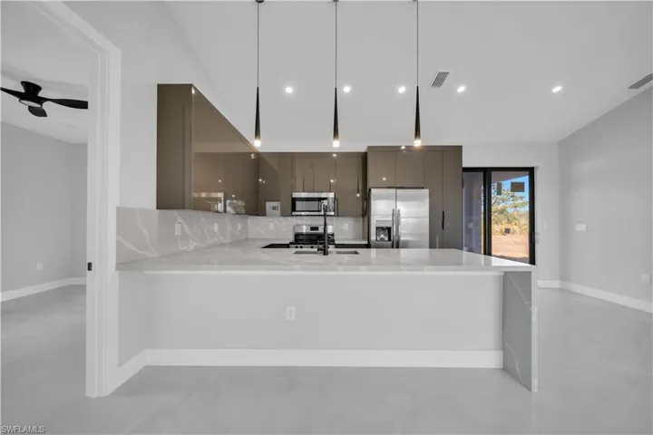 Kitchen with modern cabinets, light stone countertops, stainless steel appliances, a peninsula, and vaulted ceiling