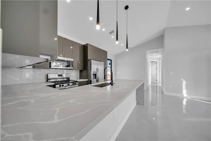 Kitchen with modern cabinets, light stone counters, stainless steel appliances, a peninsula, and hanging light fixtures