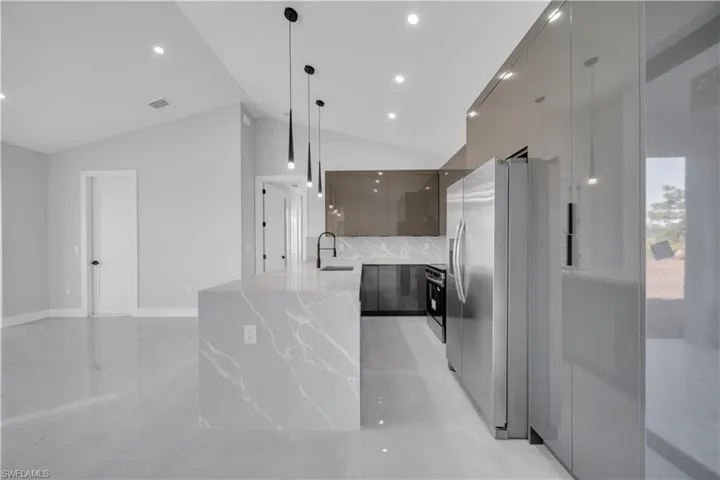 Kitchen featuring modern cabinets, light stone countertops, stainless steel appliances, decorative light fixtures, and vaulted ceiling