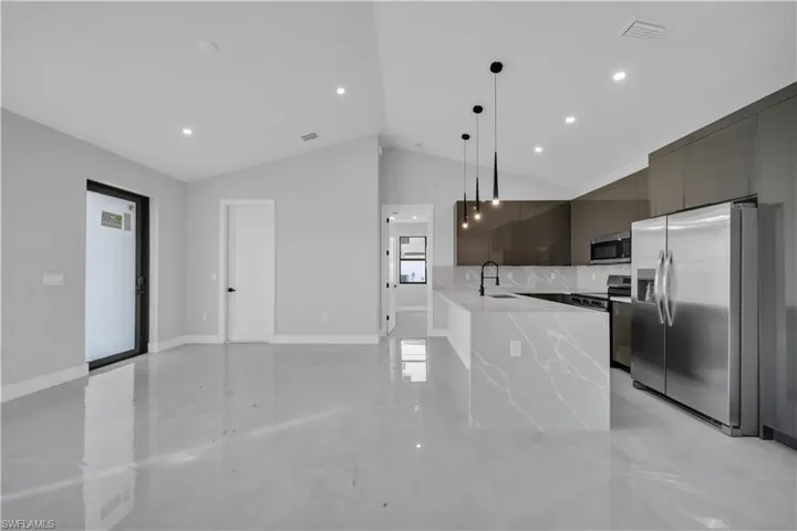 Kitchen featuring modern cabinets, stainless steel appliances, light stone counters, hanging light fixtures, and vaulted ceiling