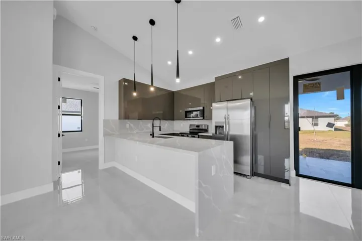 Kitchen with stainless steel appliances, a peninsula, modern cabinets, light stone counters, and decorative light fixtures