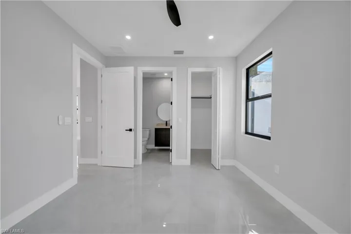 Unfurnished bedroom featuring recessed lighting, concrete flooring, a walk in closet, a ceiling fan, and ensuite bath