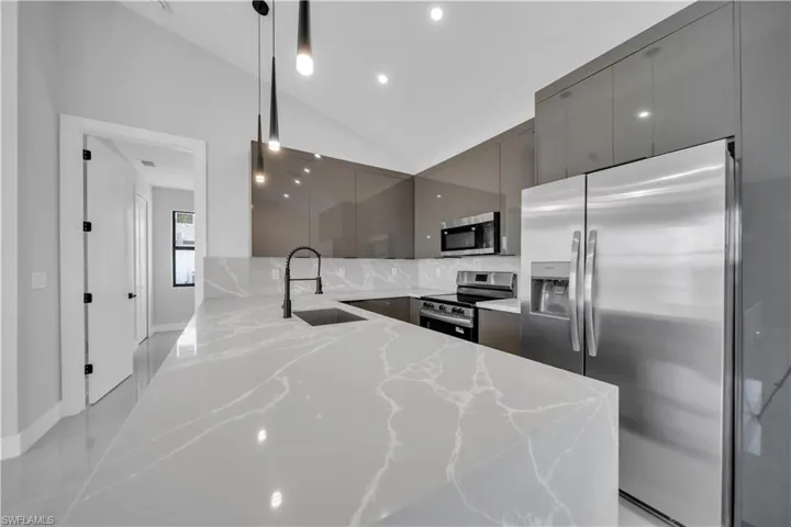 Kitchen featuring stainless steel appliances, light stone counters, lofted ceiling, modern cabinets, and gray cabinets