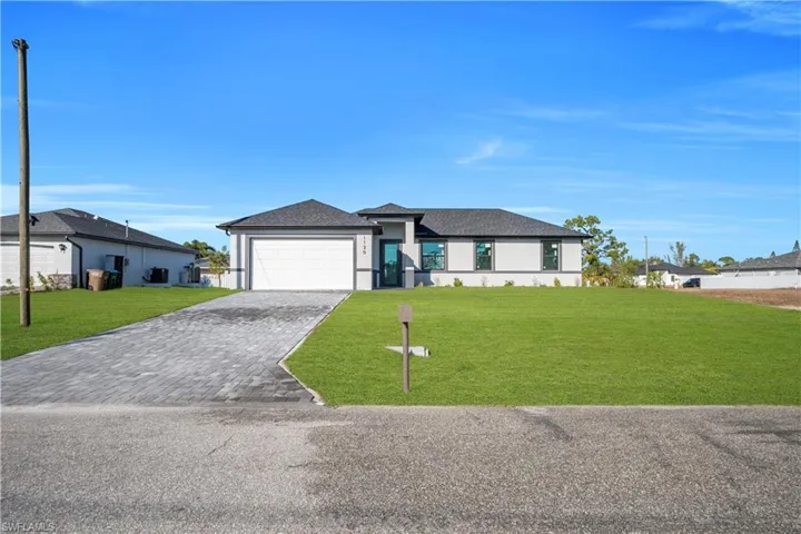 View of front facade with a yard, decorative driveway, a garage, and stucco siding