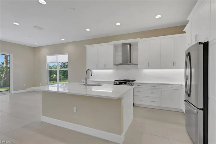 Kitchen featuring stainless steel appliances, tasteful backsplash, wall chimney range hood, recessed lighting, and a center island with sink