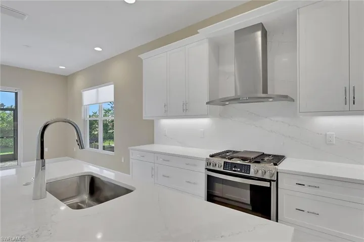 Kitchen featuring extractor fan, stainless steel gas range oven, white cabinetry, tasteful backsplash, and recessed lighting
