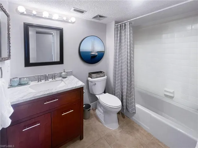 Full bath with vanity, a textured ceiling, shower / bath combo with shower curtain, and light tile patterned floors