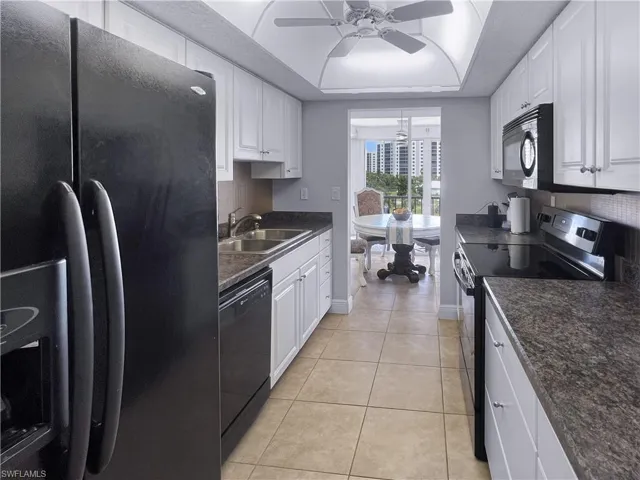 Kitchen featuring black appliances, a tray ceiling, light tile patterned floors, and white cabinetry
