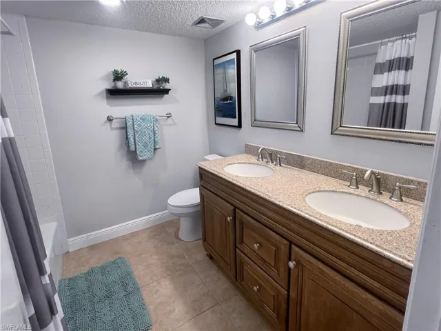 Bathroom with a textured ceiling, double vanity, shower / bath combination with curtain, and light tile patterned floors