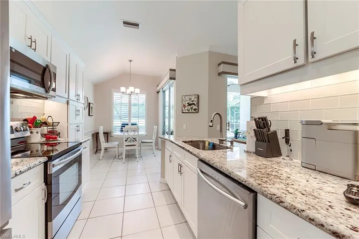 Kitchen featuring appliances with stainless steel finishes, a sink, a chandelier, backsplash, and white cabinets