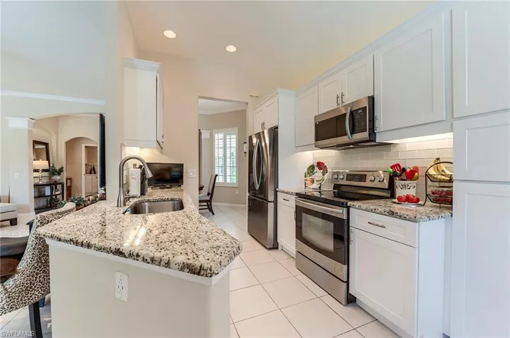 Kitchen with appliances with stainless steel finishes, a sink, arched walkways, decorative backsplash, and light tile patterned floors
