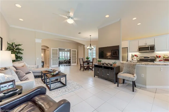 Living room featuring arched walkways, a ceiling fan, a chandelier, light tile patterned floors, and ornamental molding