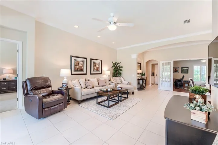 Living area with ceiling fan, arched walkways, ornamental molding, light tile patterned flooring, and recessed lighting