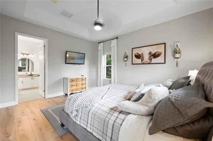 Bedroom with a raised ceiling, wood-type flooring, and ensuite bath