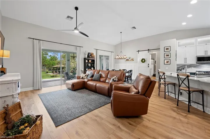 Living area featuring a barn door, light wood-style flooring, vaulted ceiling, a ceiling fan, and recessed lighting