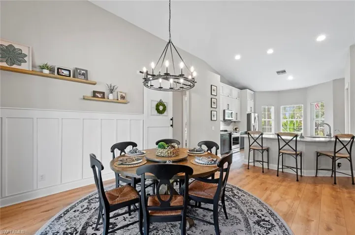 Dining room featuring vaulted ceiling, light wood finished floors, a chandelier, a wainscoted wall, and a decorative wall
