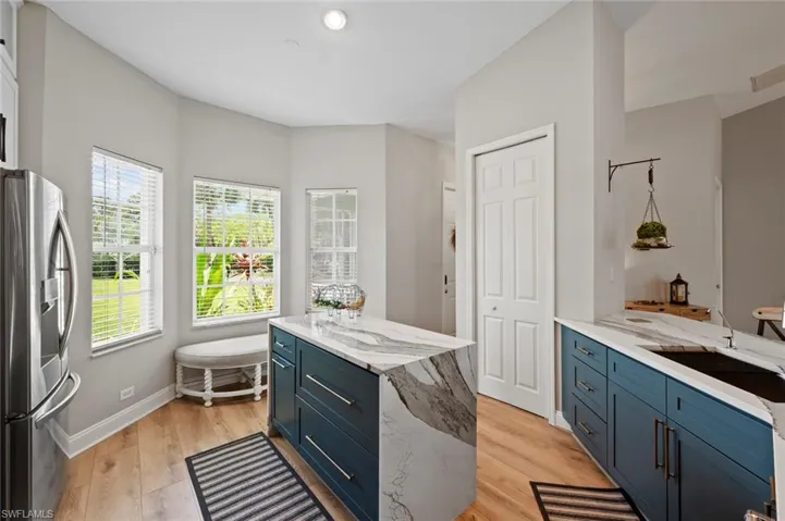 Kitchen with light stone countertops, stainless steel fridge, blue cabinetry, light wood finished floors, and a kitchen island