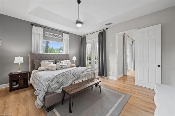 Bedroom featuring access to outside, a raised ceiling, light wood-style floors, and french doors
