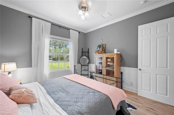 Bedroom with ornamental molding, wood finished floors, and a wainscoted wall