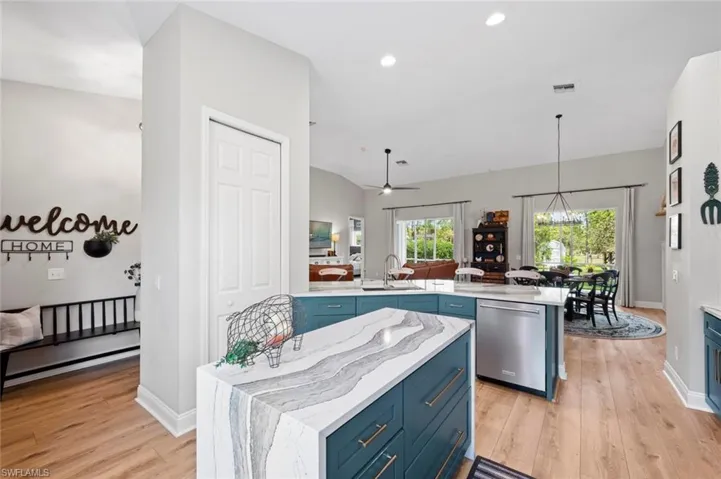 Kitchen with blue cabinets, light stone counters, light wood finished floors, stainless steel dishwasher, and ceiling fan