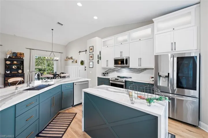 Kitchen with light stone counters, stainless steel appliances, glass insert cabinets, white cabinetry, and decorative light fixtures